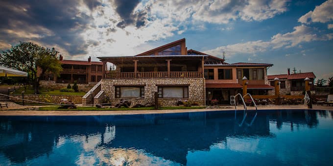 Stone and wood hotel building with outdoor swimming pool reflecting dramatic cloudy sky