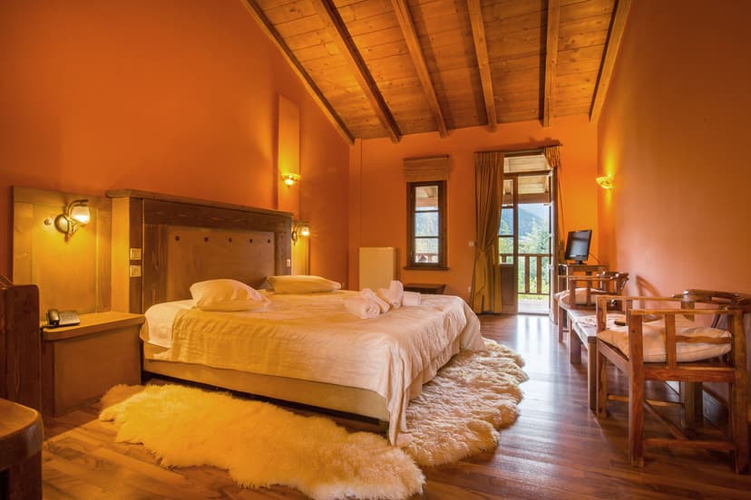 Cozy hotel bedroom with orange walls, wood ceiling, and balcony view of mountains.