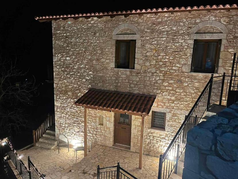 Stone house exterior illuminated at night with tiled entryway and exterior stairs in a village setting.