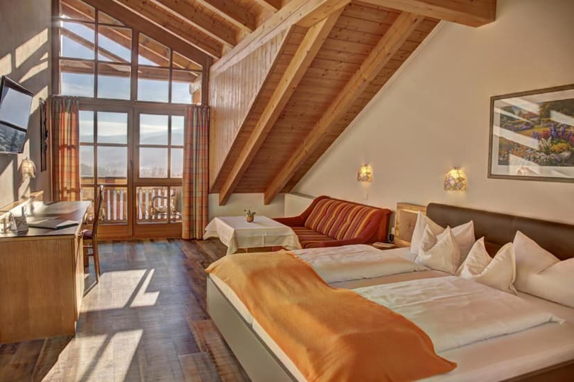 Hotel room with vaulted wooden ceiling, twin beds, and balcony view of mountains.