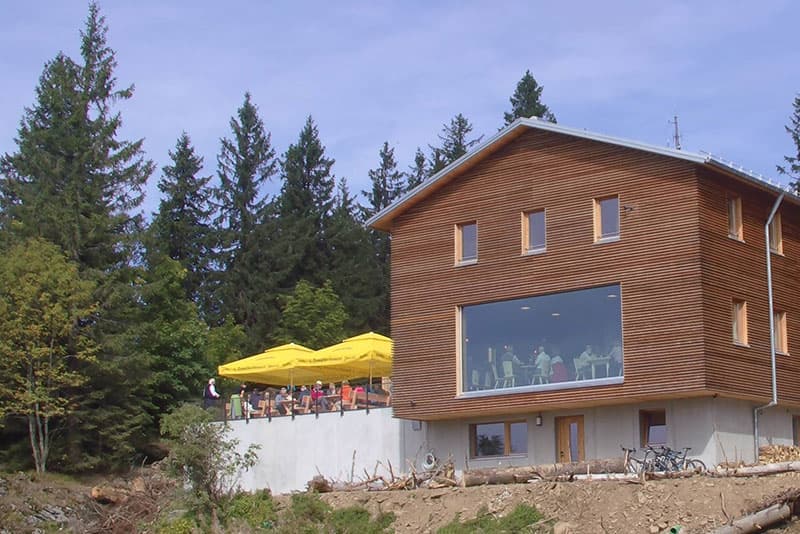 Falkenstein Schutzhaus with wooden facade and outdoor terrace surrounded by dense pine forest