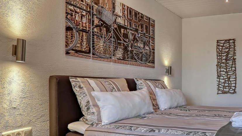 Bedroom with brown headboard, striped bedding, bicycle art, and wall sconces