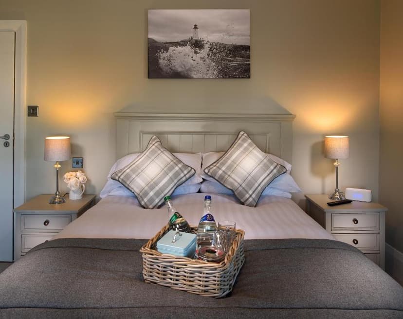 Bedroom with double bed, plaid pillows, bedside lamps, and welcome basket on duvet