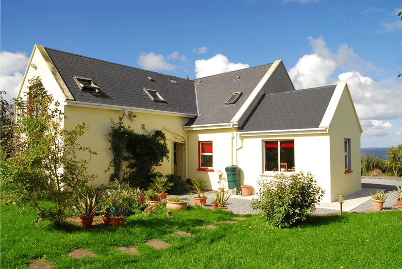 Yellow house with dark roof, garden, and ocean view under blue sky