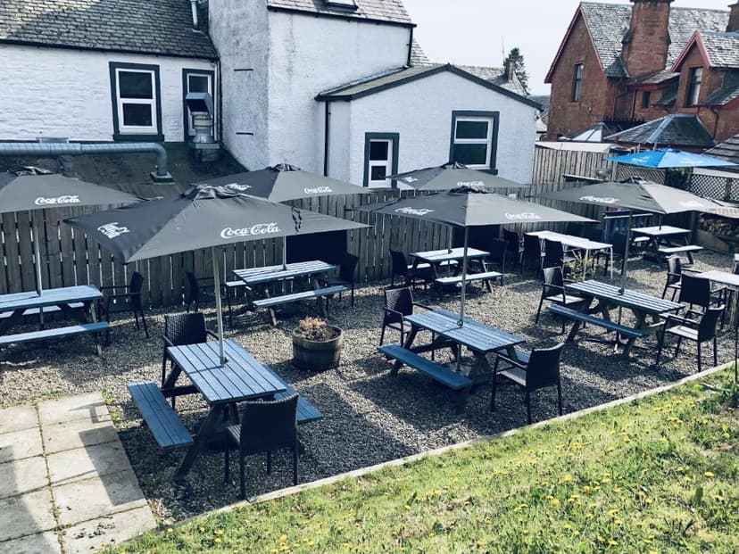 Outdoor seating area for The Drymen Inn with blue picnic tables and black Coca-Cola umbrellas.