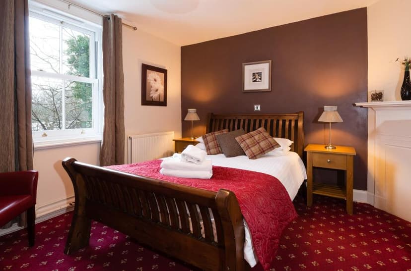 Hotel bedroom with wooden sleigh bed, red quilt, and window view of bare tree branches.