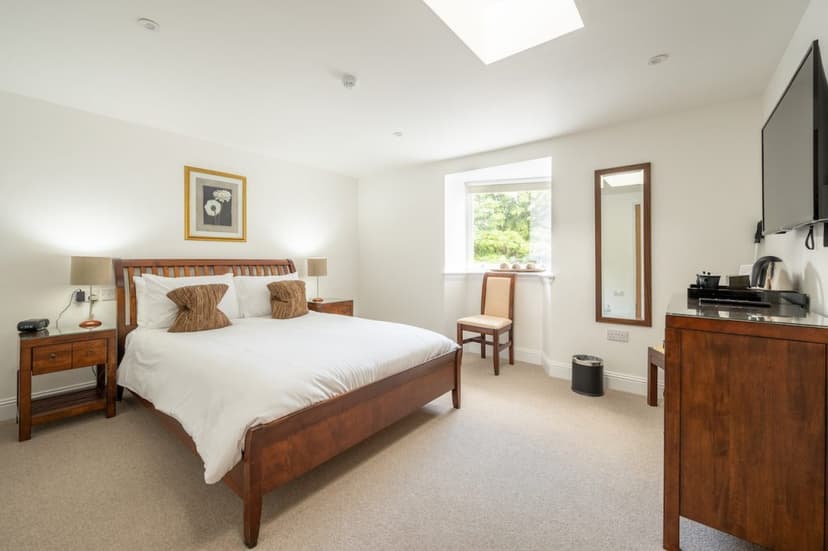 Bright hotel bedroom with wooden sleigh bed, white linens, and window view of green trees.