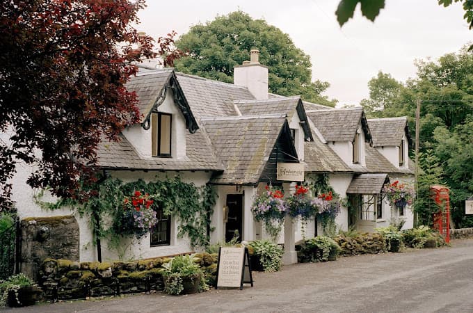 Ardeonaig Hotel with white walls, slate roof, and hanging flower baskets, next to a red telephone box.