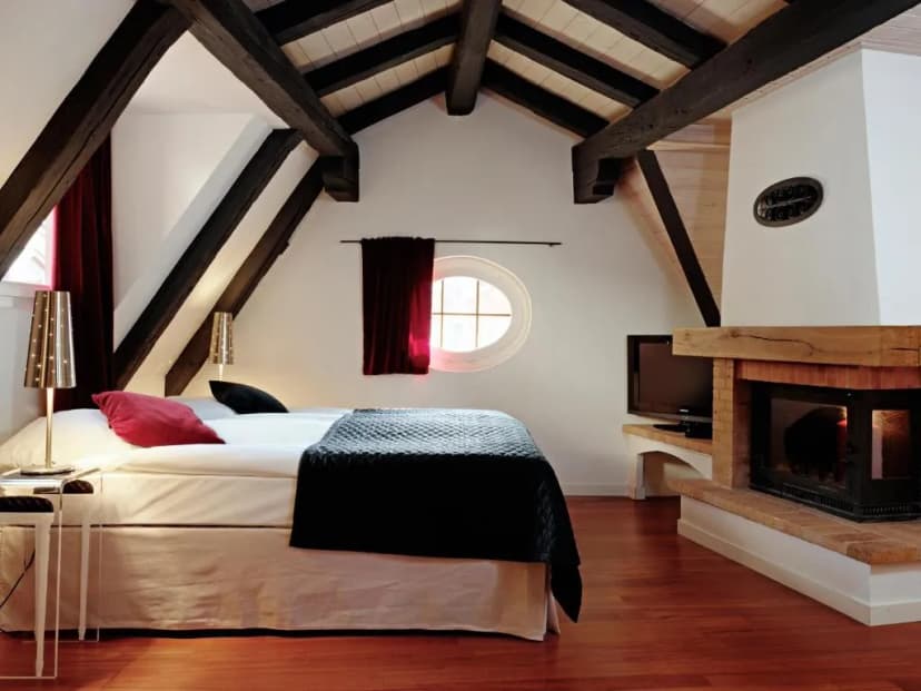 Attic hotel room with exposed dark wood beams, white walls, fireplace, and Tralala Hotel Montreux branding implied by file...