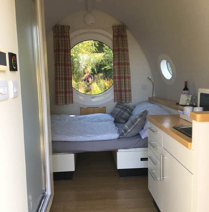 Cozy interior of a glamping pod with a bed, kitchenette, and view of greenery at Loch Tay.