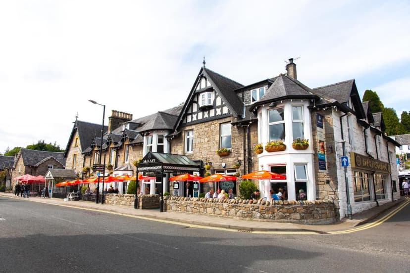Stone hotel building with outdoor seating under orange umbrellas next to a road.