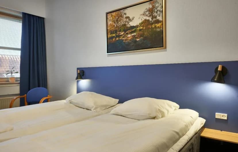 Twin beds with white linens, blue headboard, and framed autumn landscape art at BB Hotel Rønne.