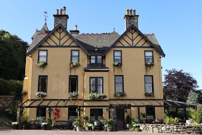 The Craigellachie Hotel, a yellow building with dark trim and flower boxes, under a clear blue sky.