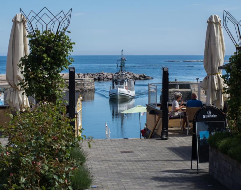 Boat entering harbor past outdoor cafe seating at Hotel Siemsens Gaard, Svaneke.
