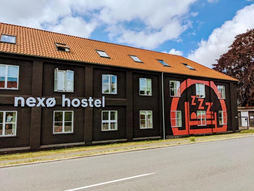 Nexø Hostel building exterior with black facade, orange roof, and large red graphic under blue sky.