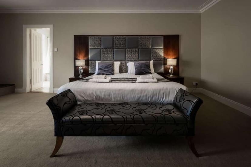 Hotel bedroom with large bed, patterned headboard, bedside lamps, and dark upholstered bench.