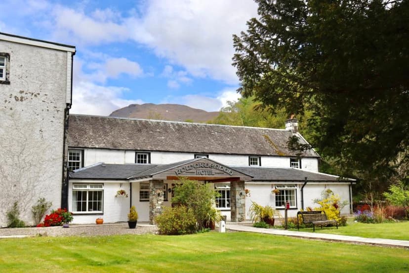 Rowardennan Hotel building with green lawn, mountain backdrop, and blue sky.