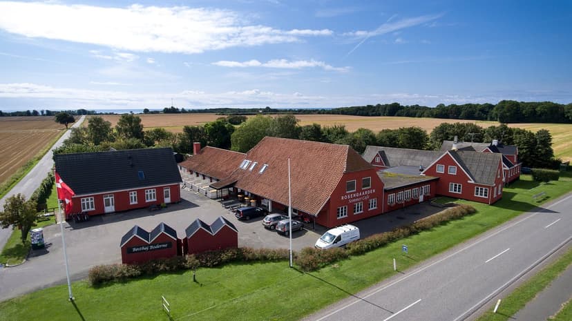 Rosengaarden Sommer Cafe buildings in a rural setting with fields and a road under a blue sky.