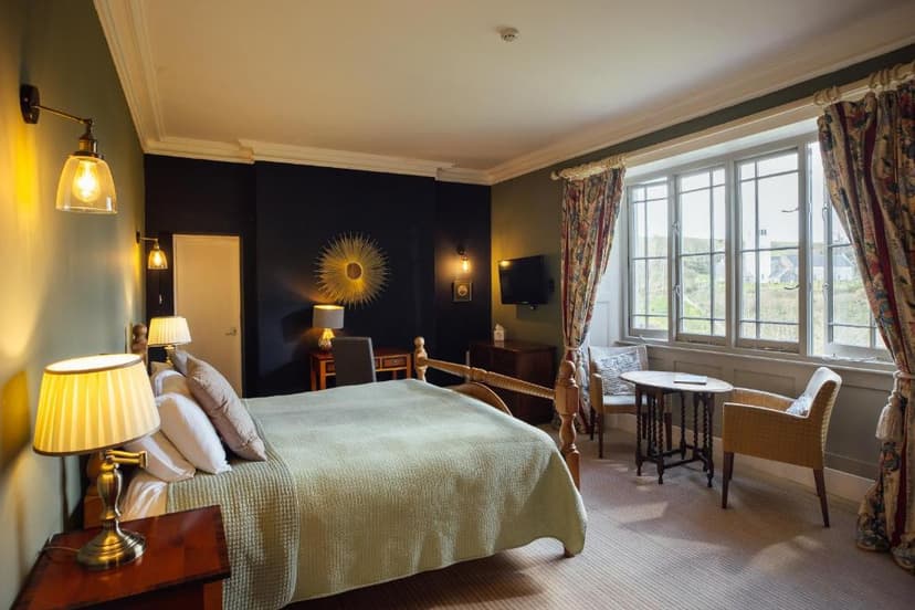 Bedroom with wooden four-poster bed, patterned curtains, and view of green hillside.