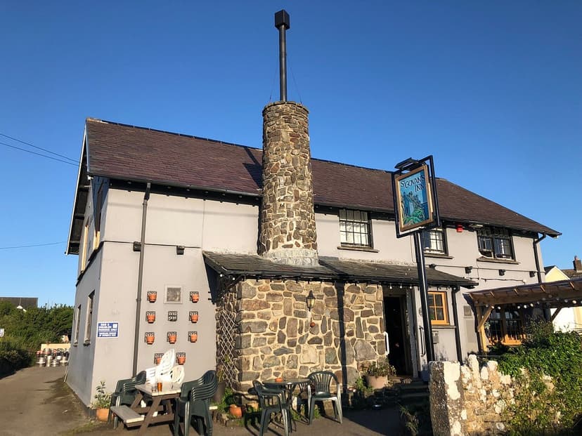 St. Govan's Inn pub with stone chimney and outdoor seating under clear blue sky.