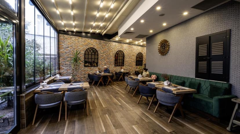 Restaurant dining area with brick wall, green velvet seating, and large windows overlooking greenery.