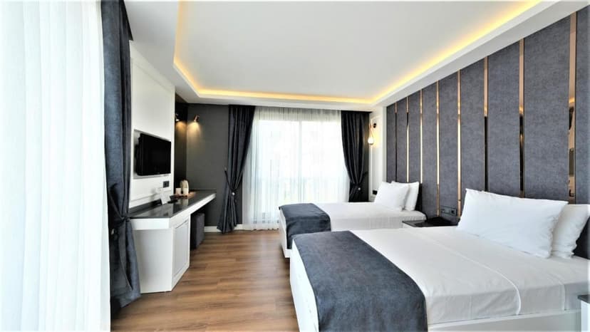 Modern hotel room with twin beds, dark gray accents, and wood flooring at Mai İnci Otel.