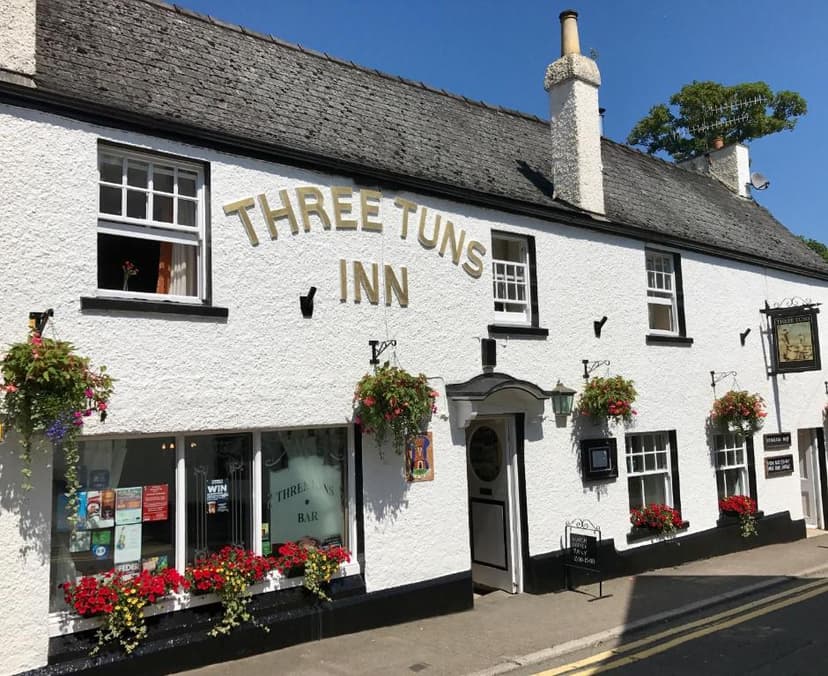 White stucco pub, The Three Tuns Inn, with hanging flower baskets on a sunny day.
