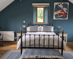 Bedroom with dark blue walls, a metal frame bed, and colorful abstract art above the window.