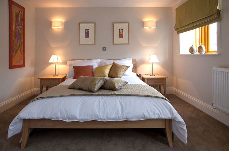 Cozy bedroom with wooden bed frame, white linens, and warm lighting from bedside lamps.