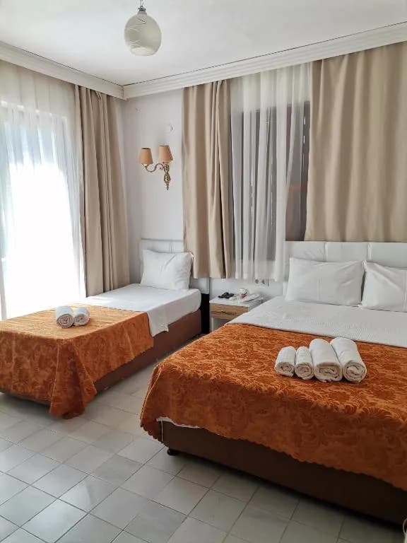 Hotel room with one double and one single bed, orange bedspreads, and sheer curtains in Adrasan Shambala Hotel.