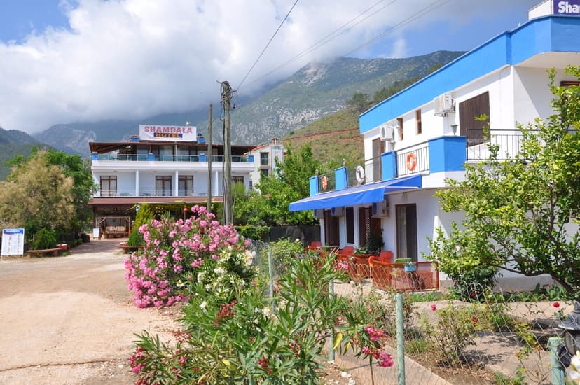 Shambala Hotel buildings with blue trim, flowering bushes, and mountains in background at Adrasan.