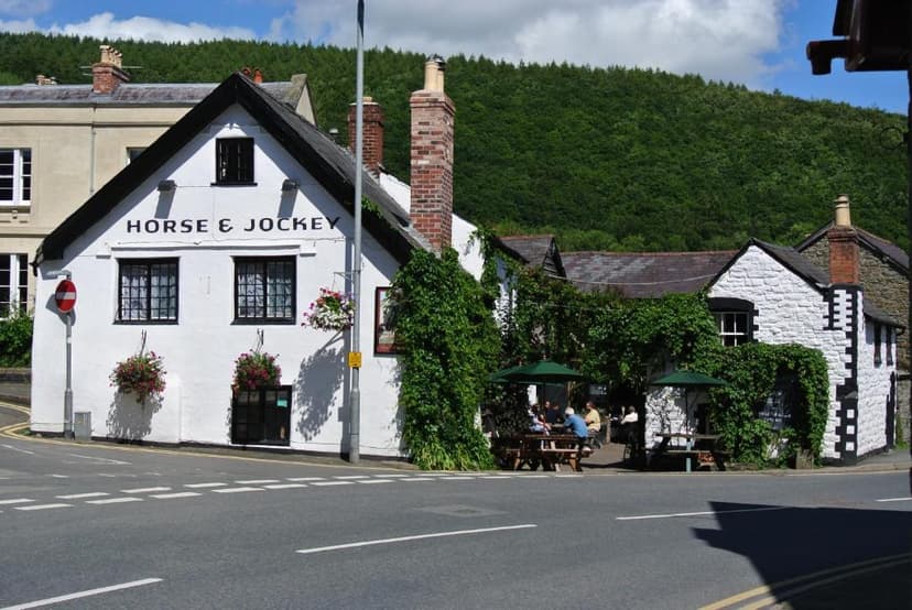 Horse & Jockey Inn with white facade and outdoor seating against a steep, forested hill.