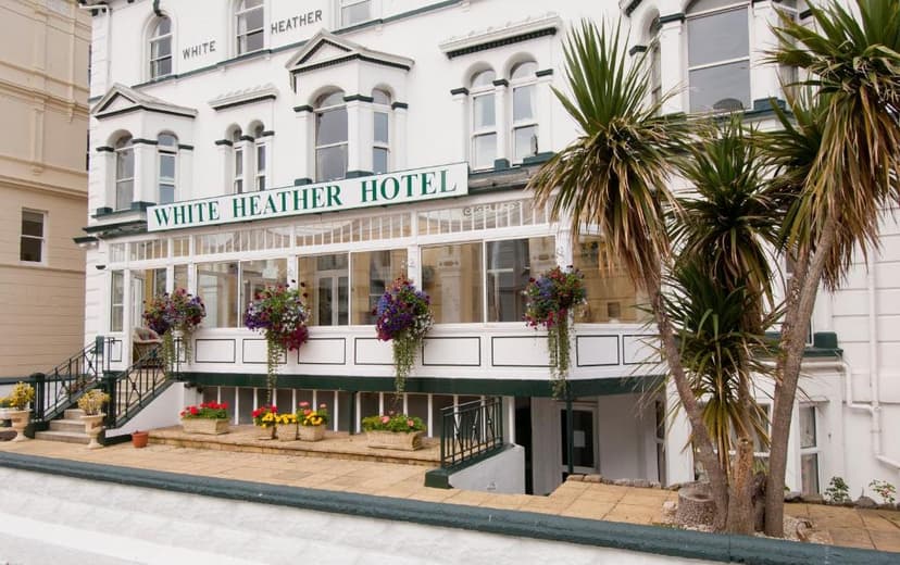 White Heather Hotel exterior with white facade, glass conservatory, and palm trees.