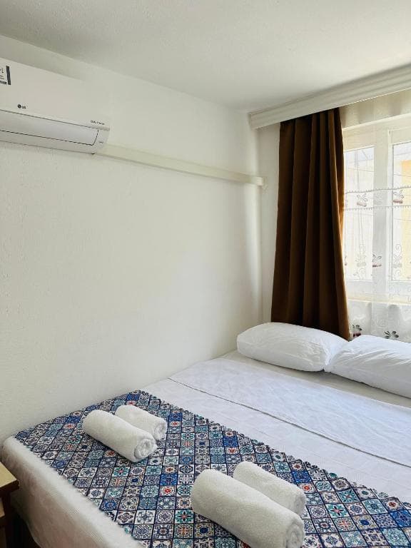 Gelidonya Pansiyon room with white walls, air conditioner, and bed with patterned runner and towels.