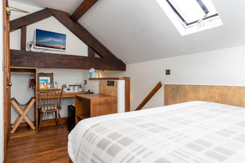 Bedroom with exposed wooden beams, skylight, and plaid duvet in an attic space.