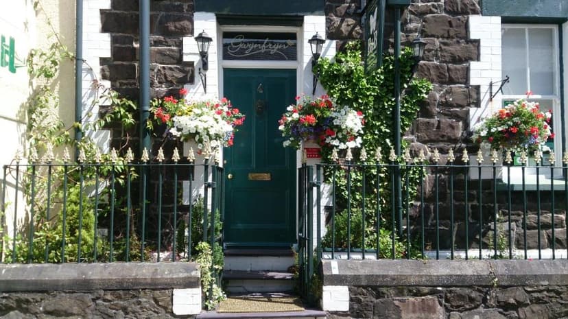 Entrance to Gwynfryn B&B with dark stone facade, green door, and hanging flower baskets.