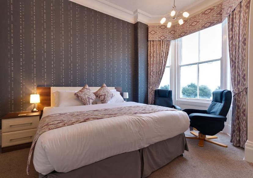 Bedroom with large bed, patterned wallpaper, and bay window seating at Lauriston & Lawton Court Hotel.