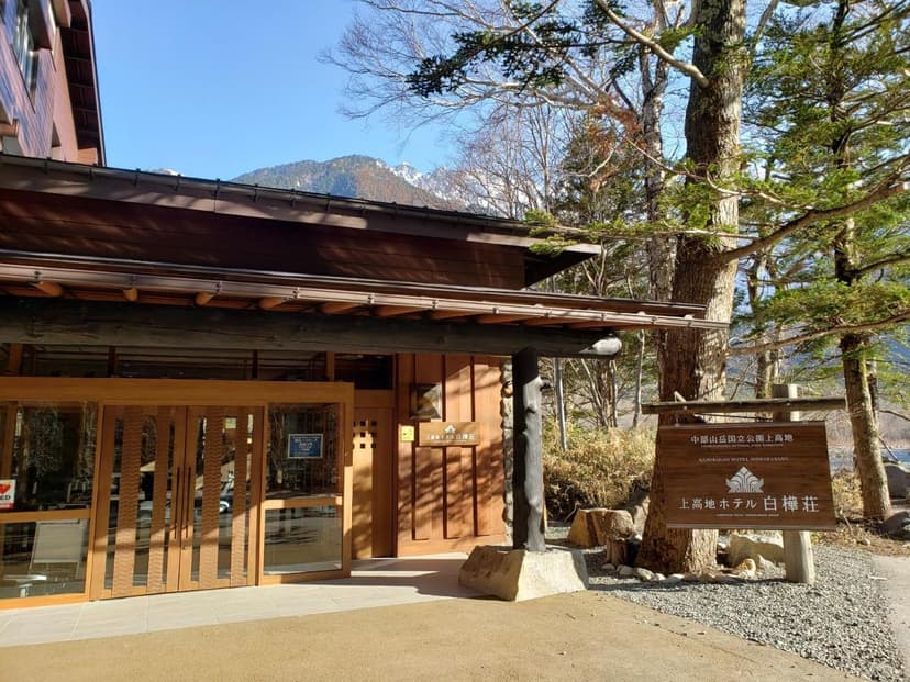 Kamikochi Hotel Shirakabaso entrance with wooden architecture and snowy mountains visible.