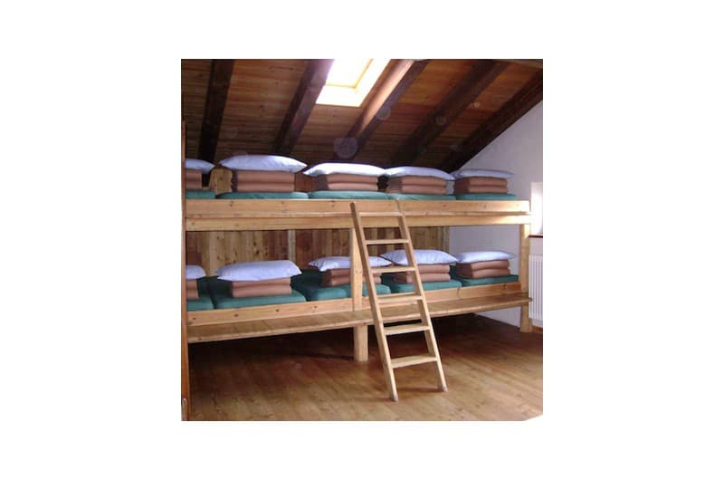 Wooden bunk beds with neatly stacked bedding under a slanted wooden ceiling in a Rifugio Bertone room.
