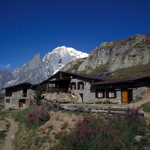 Stone mountain refuge with snow-capped peaks and clear blue sky, Rifugio Bertone