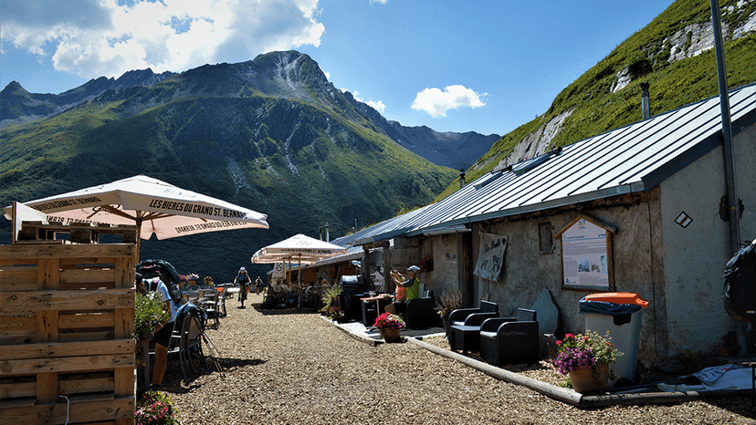 Alpage de La Peule outdoor seating area with cyclists and massive green mountains under blue sky.