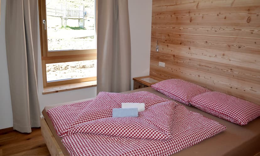 Bedroom with wooden headboard, red gingham bedding, and window view of grassy slope.