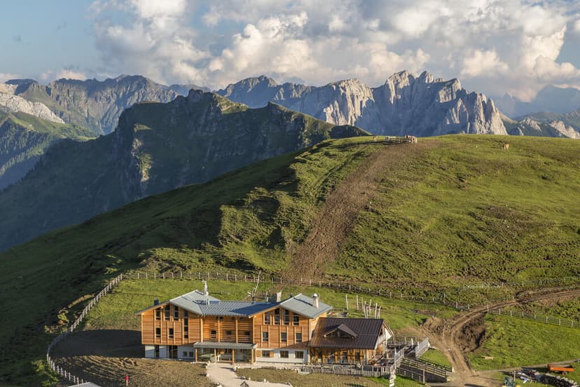 Rifugio Sasso Piatto wooden lodge nestled on grassy alpine slope below jagged mountains.