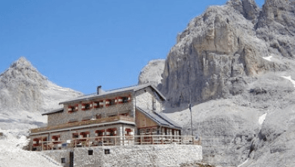 Rifugio Pradidali stone mountain hut with terrace set against towering, rocky peaks under a clear blue sky.