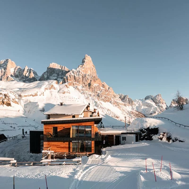 Wooden lodge in deep snow with rugged, sunlit mountains in the background