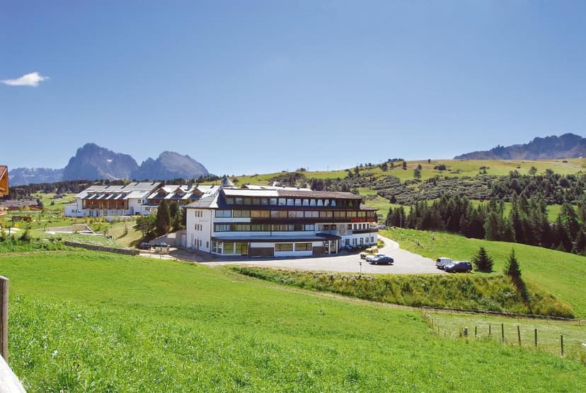 Hotel Piccolo Sciliar in grassy mountain landscape with rugged peaks under blue sky.