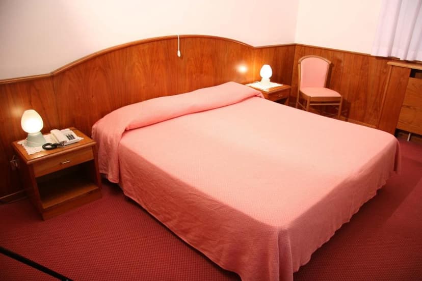 Hotel room with pink bedspread, wood paneling, and bedside lamps near Cividale.