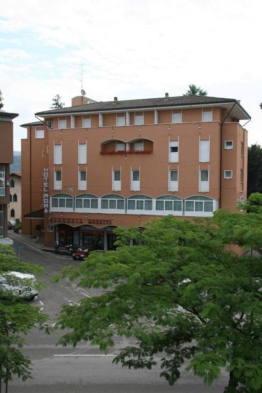 Hotel Roma building facade seen from behind green trees in Cividale.