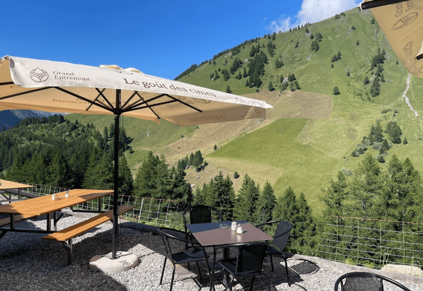 Outdoor dining area with umbrella overlooking green alpine mountainside in summer