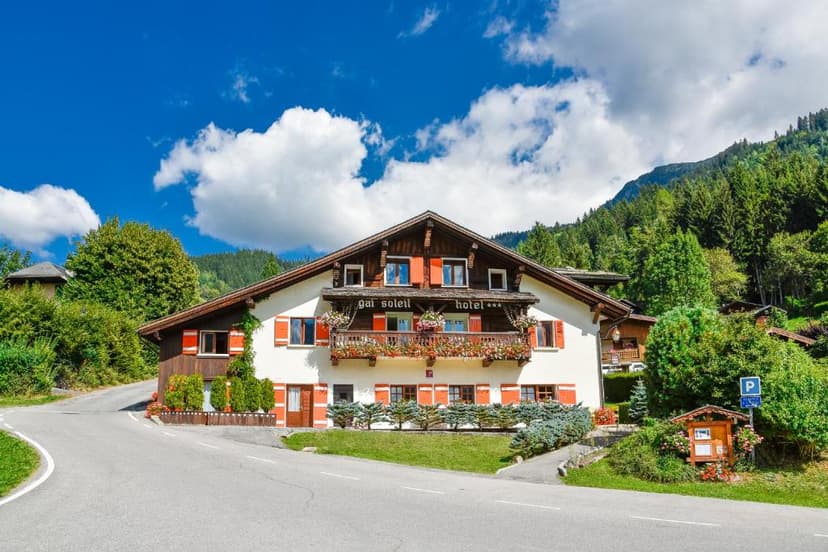 Chalet-style Hotel Gai Soleil with flower balconies against a forested mountain backdrop.
